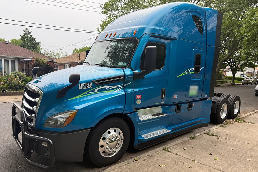 Blue Freightliner Cascadia sleeper tractor parked at a curb