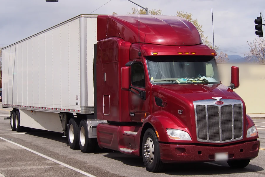 Red Peterbilt 579 sleeper tractor pulling a dry van trailer