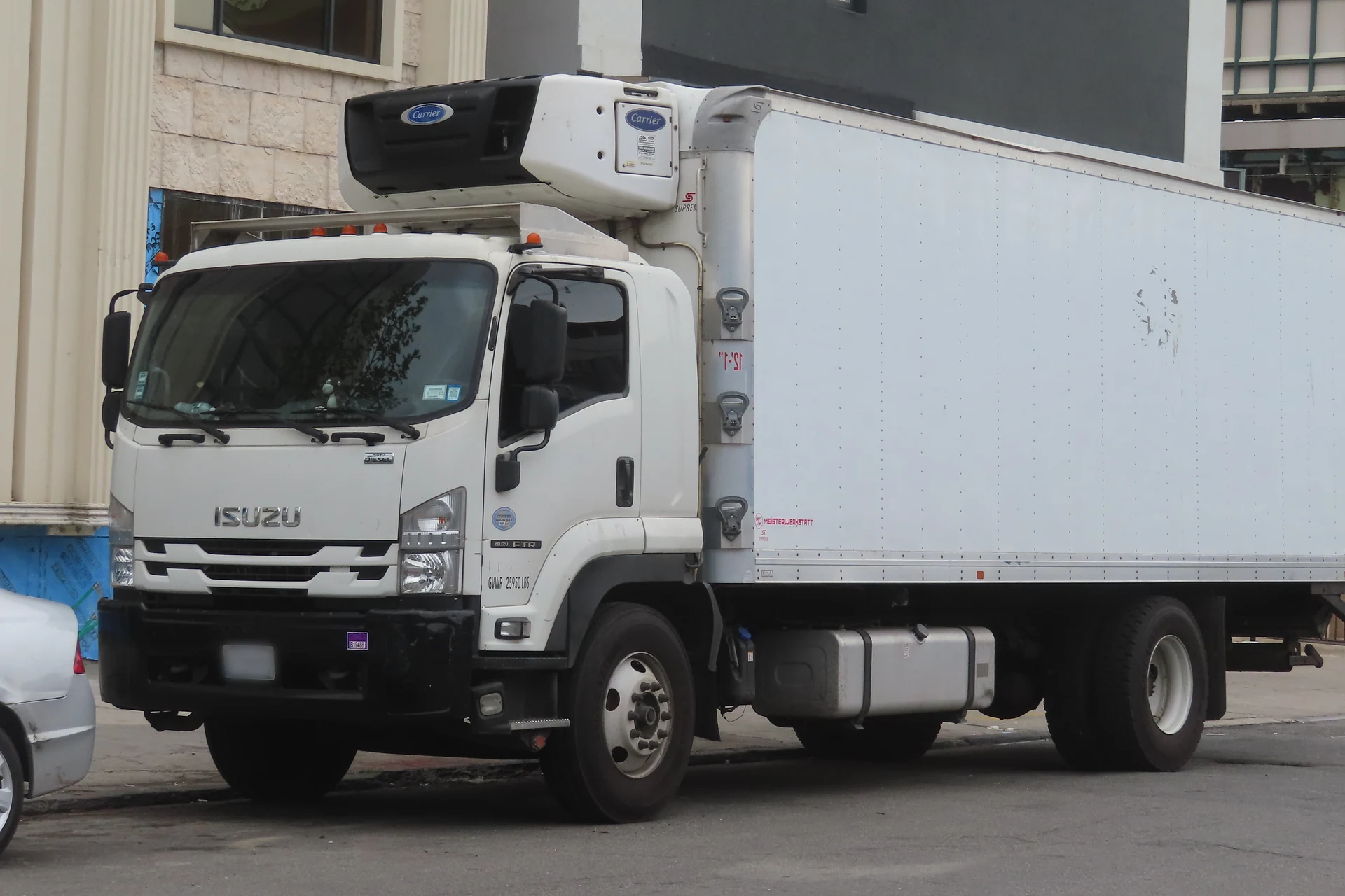 White Isuzu FTR cab-over truck with a refrigerated box, parked on a city street